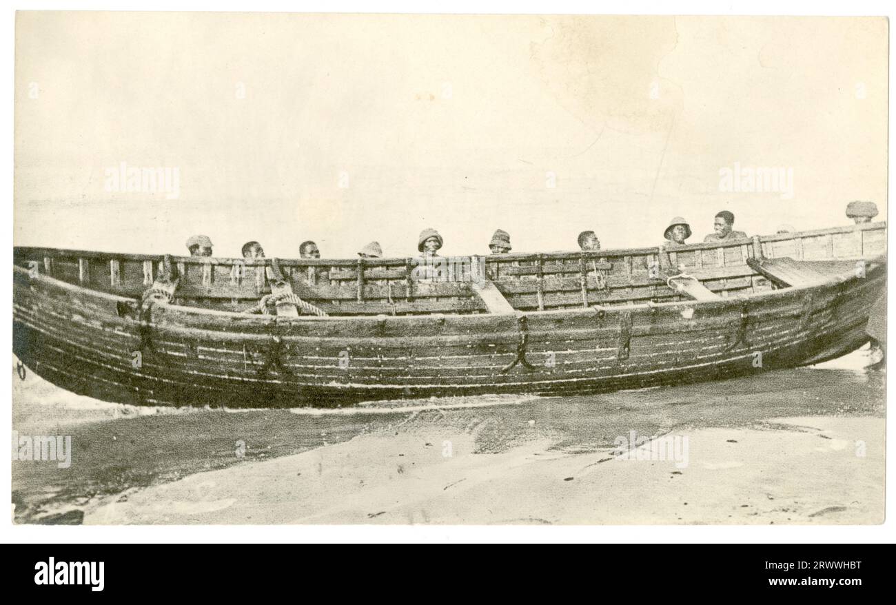 Diez hombres africanos apoyan un gran bote de remo de madera en la playa, en un lugar no identificado. Foto de stock