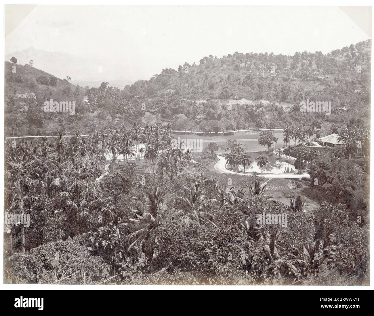 Vista mirando sobre las cumbres y el lago en Kandy, una estación de la colina cerca de Colombo. Las colinas bajas tienen palmeras densamente plantadas y exuberante follaje. Algunos edificios se pueden ver dentro de los árboles y hay un pabellón al lado del lago. El pie de foto dice: Kandy. Foto de stock