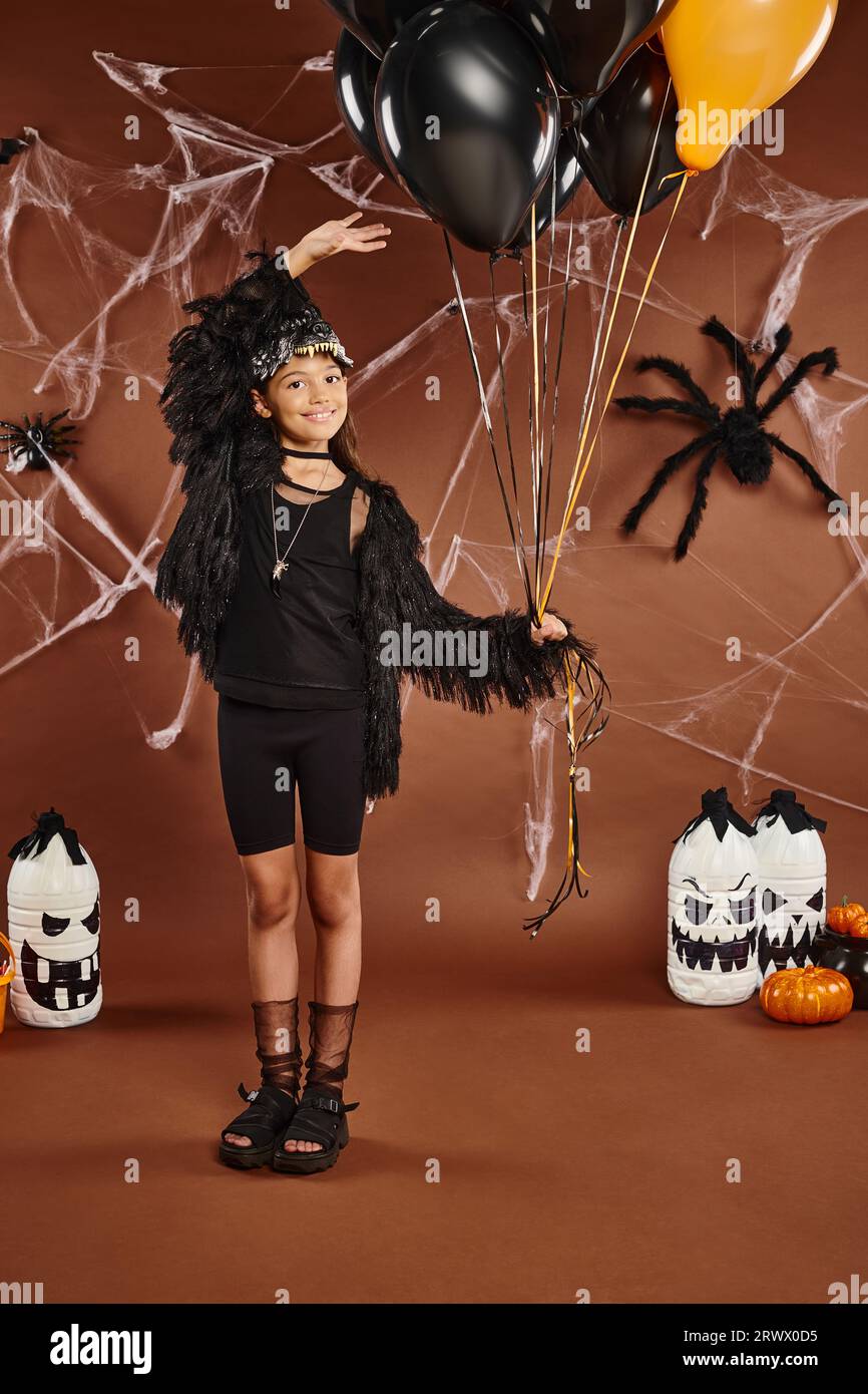 Chica alegre sostiene globos negros y naranjas y los toca con su mano, concepto de Halloween Foto de stock