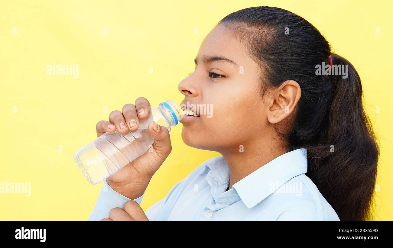 Los niños de escuela asiáticos beben agua de una botella contra el fondo del estudio. Vuelta a la escuela, concepto de estilo de vida. Régimen de bebida. Foto de stock
