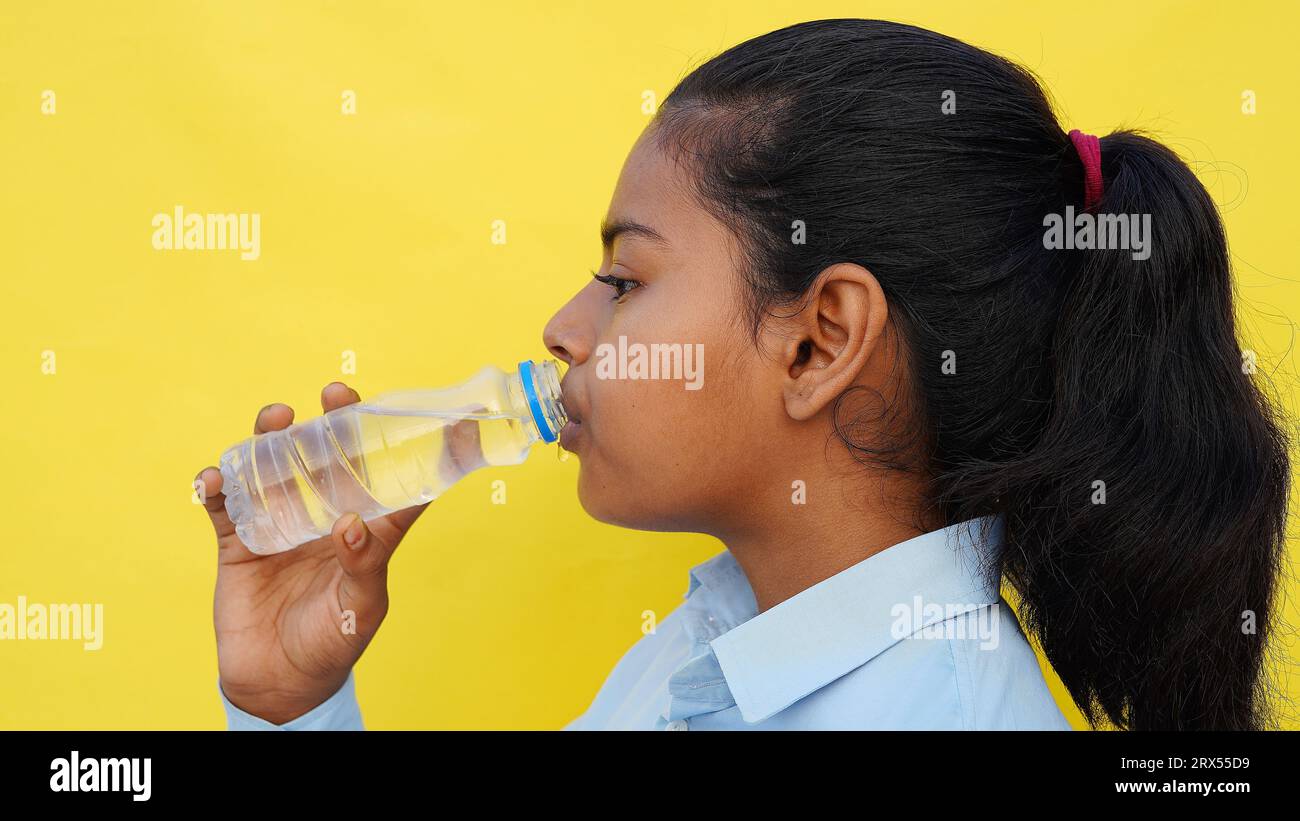 Los niños de escuela asiáticos beben agua de una botella contra el fondo del estudio. Vuelta a la escuela, concepto de estilo de vida. Régimen de bebida. Foto de stock