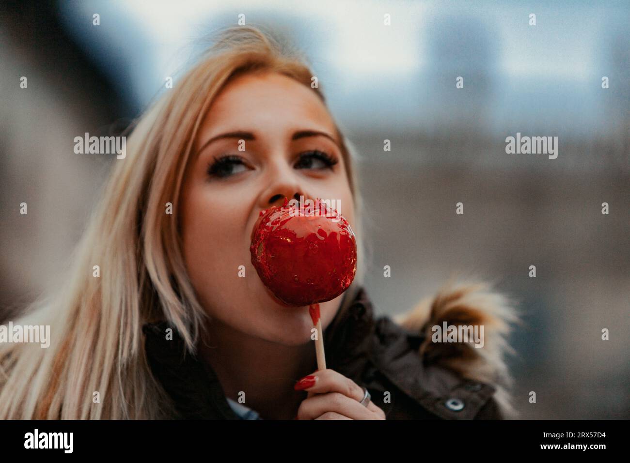 Una mujer rubia muerde una manzana de caramelo, cautivada por los monumentos artísticos y arquitectónicos que personifican el corazón de la civilización occidental. Súplica Foto de stock