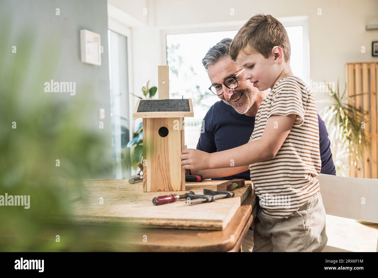 Hombre sonriente que hace pajarera de madera con nieto en casa Foto de stock