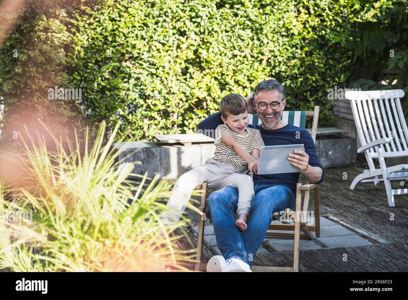 Hombre y niño felices usando la PC de la tableta que se sienta en el patio trasero Foto de stock
