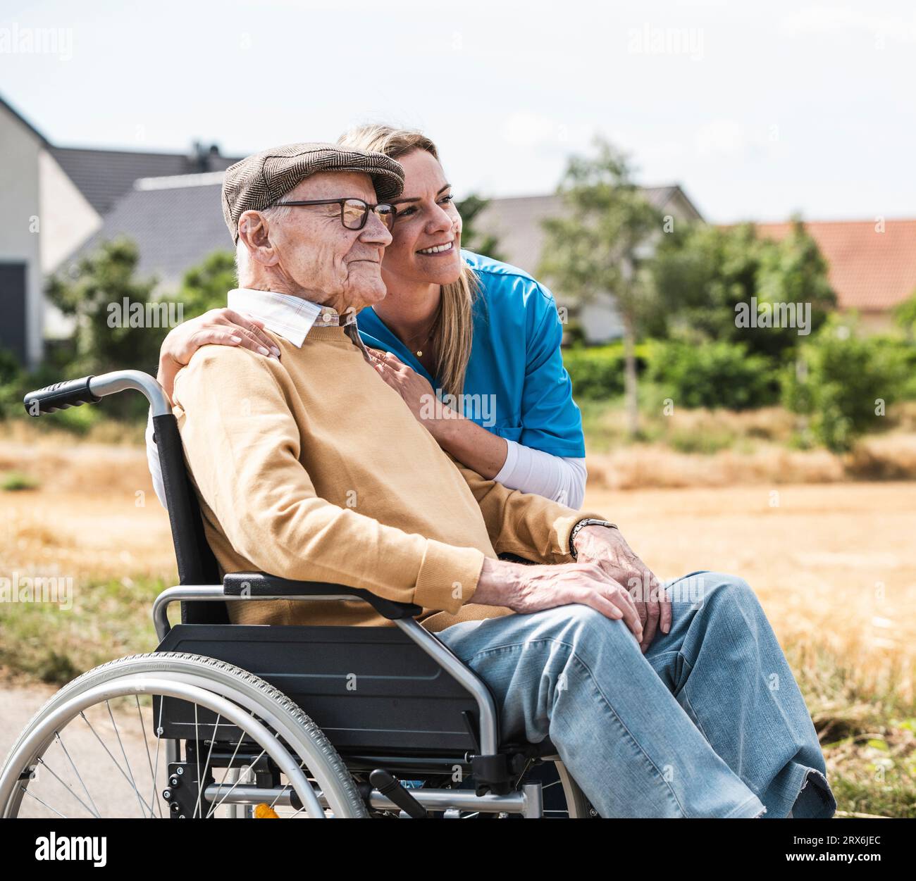 Enfermera sonriente que abraza al hombre mayor que se sienta en silla de ruedas Foto de stock