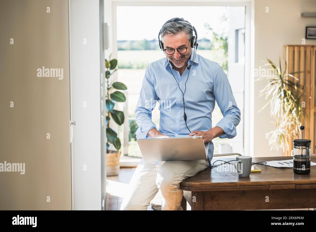 Hombre de negocios sonriente con auriculares que trabajan en el ordenador portátil en la oficina en casa Foto de stock