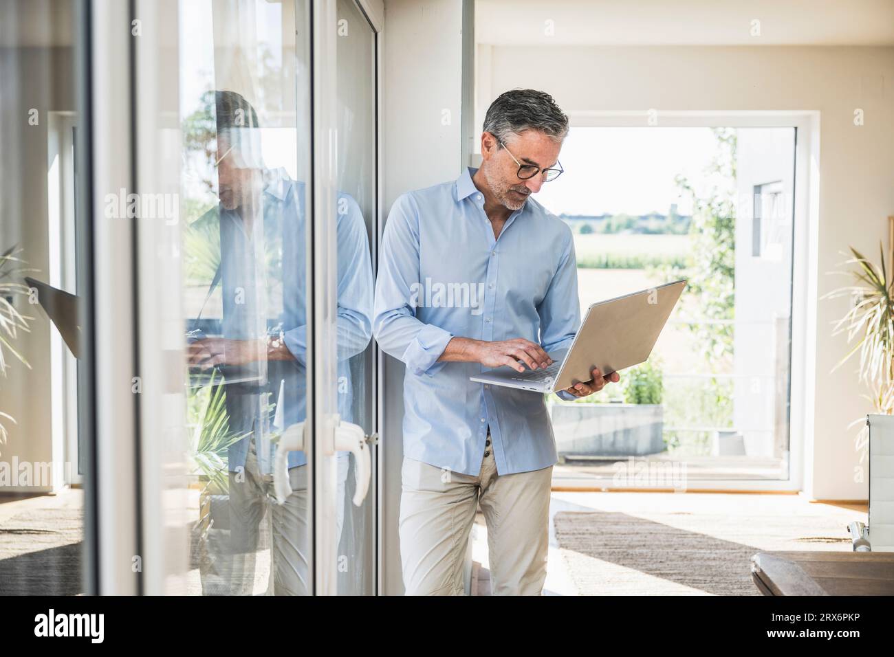 Hombre de negocios que trabaja en la computadora portátil que se apoya en la ventana en la oficina en casa Foto de stock