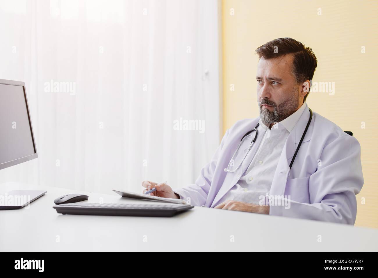 Médico profesional superior masculino en la habitación de hospital que trabaja en la mesa que escucha el estrés que mira al paciente Foto de stock