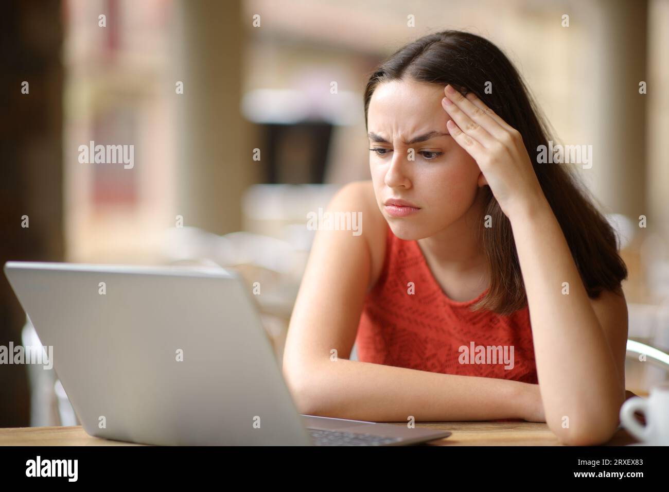 Mujer preocupada que comprueba el contenido del ordenador portátil sentado en una terraza del restaurante Foto de stock