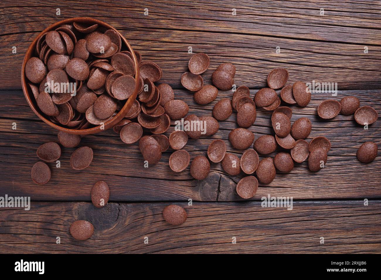 Cereales de chocolate desayuno en tazón y dispersado cerca sobre fondo de madera, vista superior Foto de stock