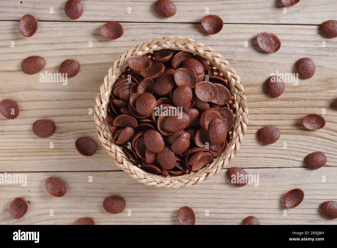 Directamente encima de la vista de los copos de maíz de chocolate en el tazón de mimbre sobre fondo de madera Foto de stock