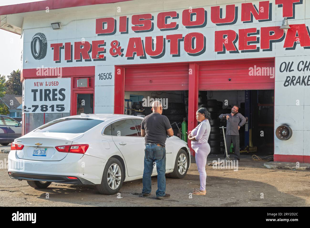 Detroit, Michigan - Una mujer habla con un mecánico mientras lleva su Chevrolet Malibu a un taller de reparación de automóviles del vecindario. Foto de stock