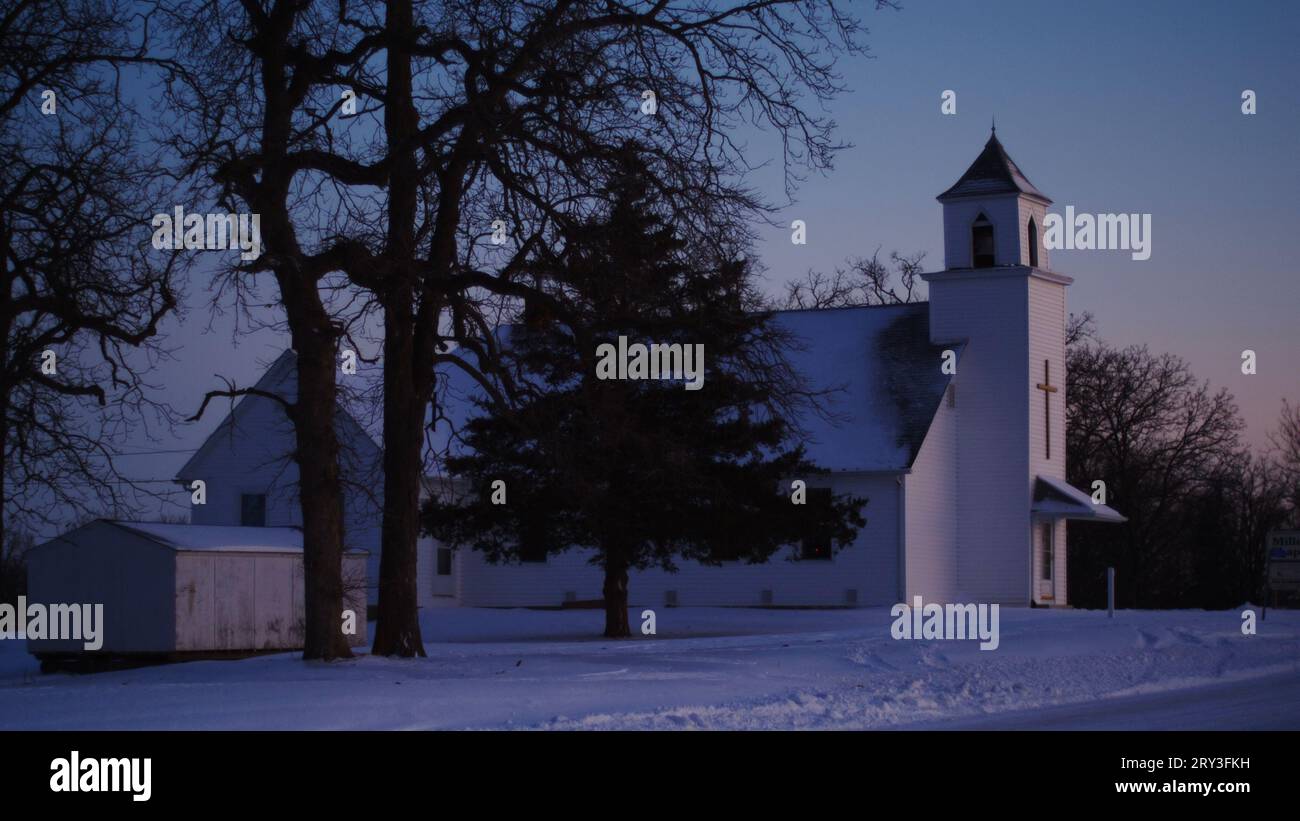 Iglesia rural del medio oeste con nieve recién caída en una noche clara en la hora mágica del atardecer. Foto de stock