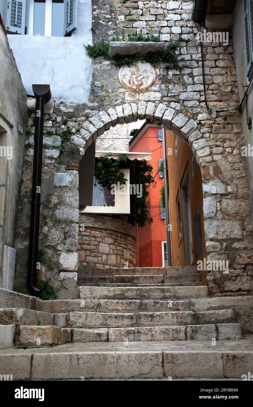 Una estrecha calle de piedra se eleva por una colina a través de un arco en un barrio en Rovinj, Croacia. Foto de stock