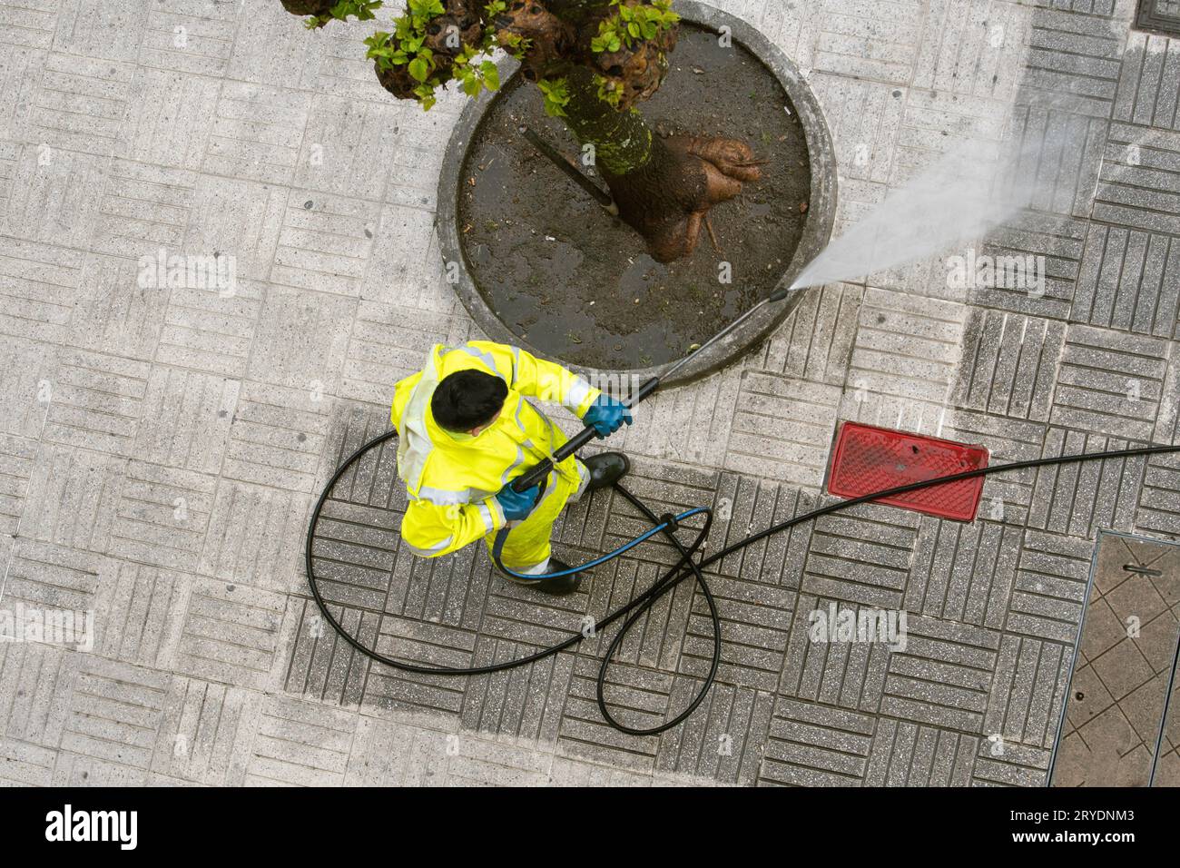 Vista superior de un trabajador que limpia la acera de la calle con chorro de agua a alta presión Foto de stock