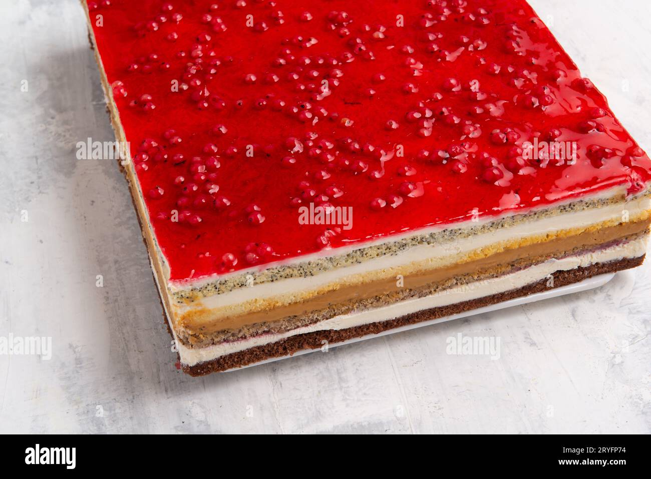 Toma angular de un pastel de varias capas con una capa de gelatina de grosella roja en la parte superior. Foto de stock