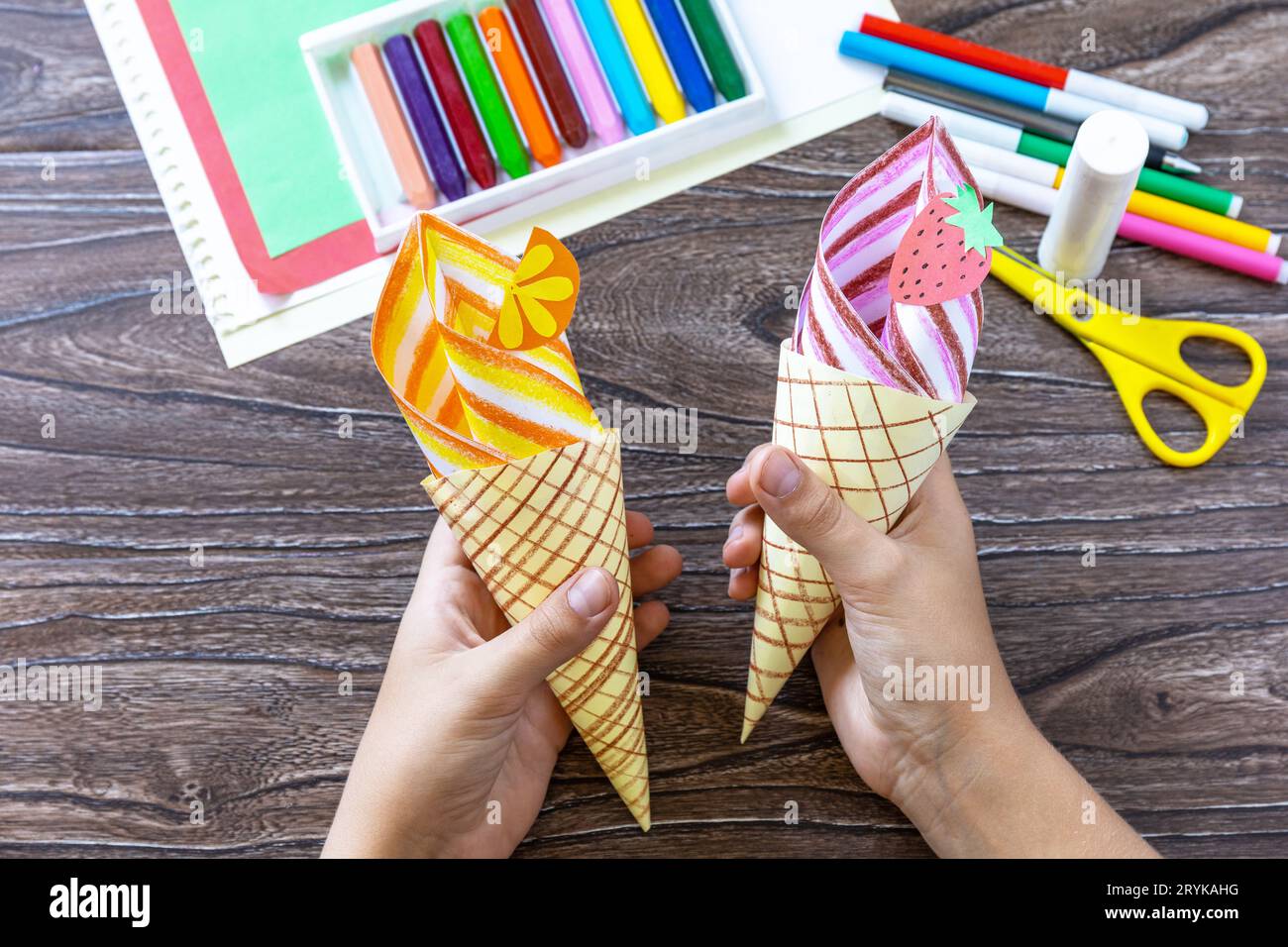 En las manos de un niño Paper Fan helado de papel en una mesa de madera. Proyecto de verano de arte infantil, hecho a mano, manualidades para niños Foto de stock