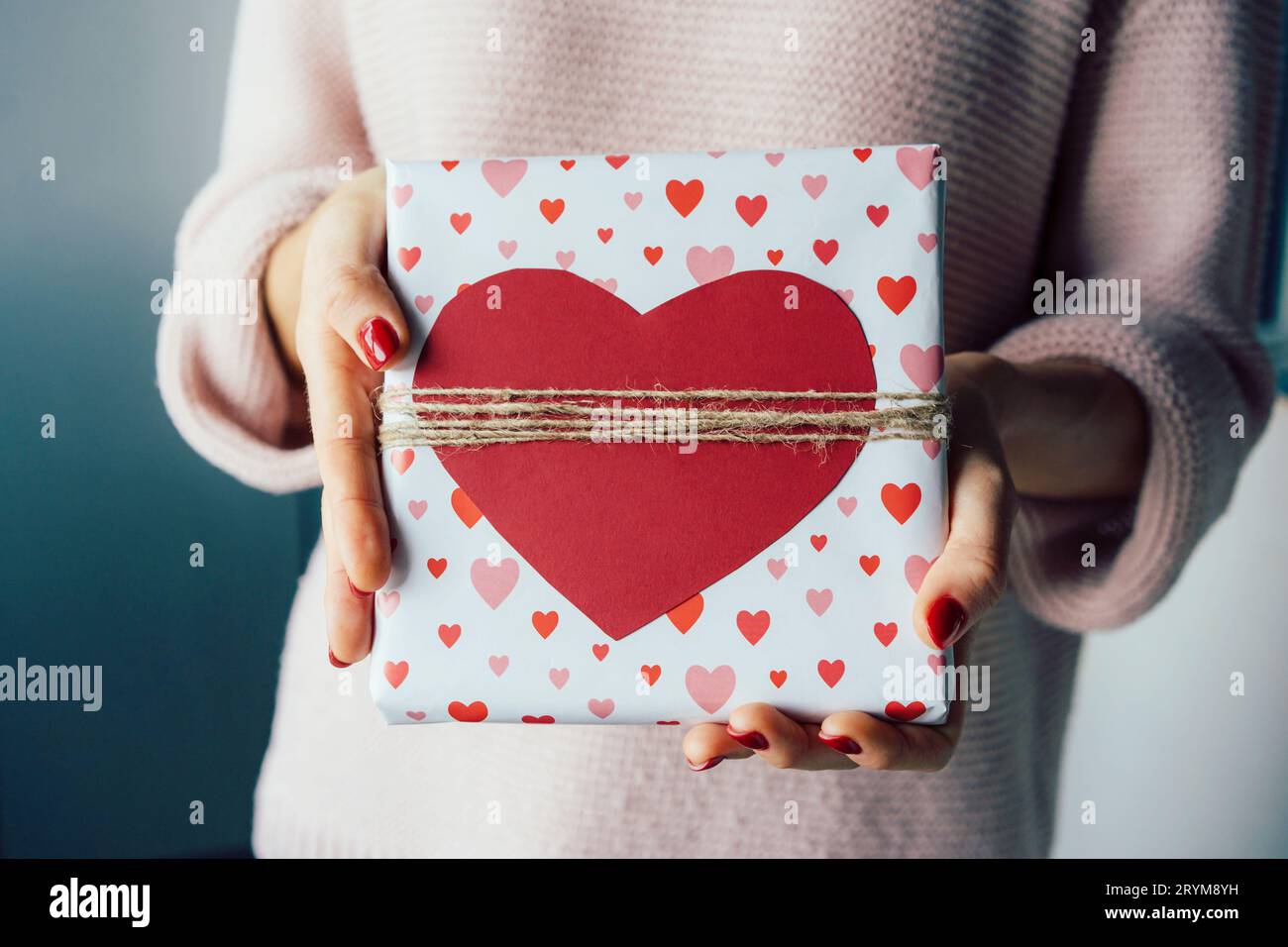 Primer plano de una caja de regalo decorada con un corazón rojo en las manos de una mujer irreconocible. Foto de stock