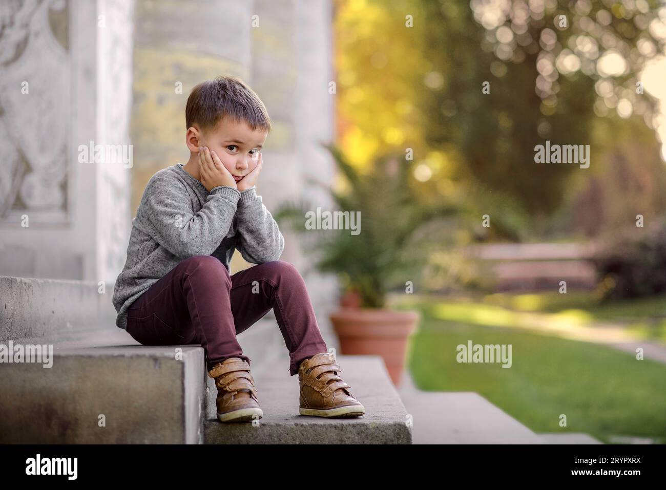 Niño triste sentado en los escalones en el parque Foto de stock