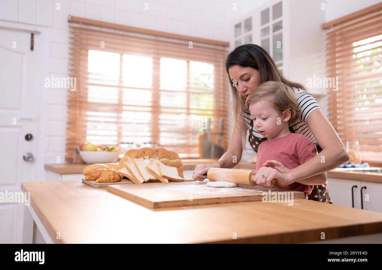 Mamá y papá en la cocina de la casa con sus hijos pequeños. Pasar un buen rato horneando pan y haciendo la cena juntos. Foto de stock