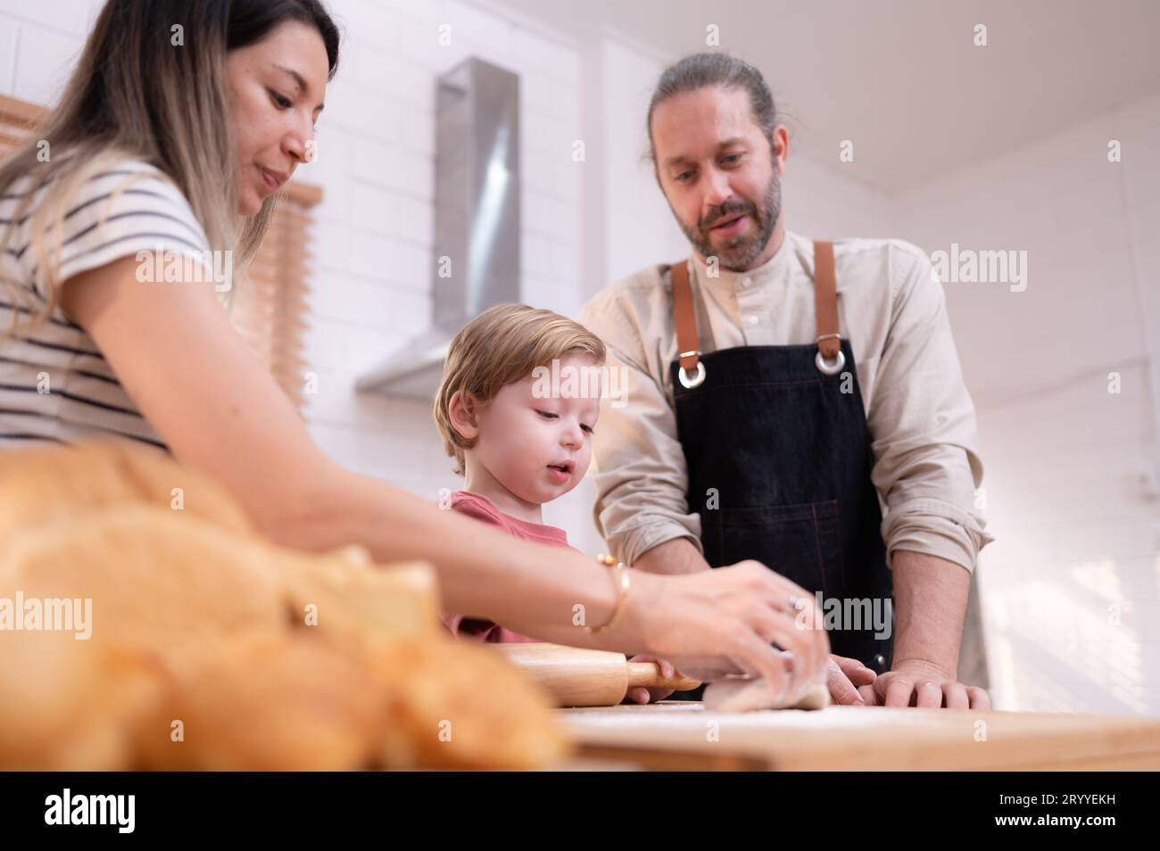 Mamá y papá en la cocina de la casa con sus hijos pequeños. Pasar un buen rato horneando pan y haciendo la cena juntos. Foto de stock