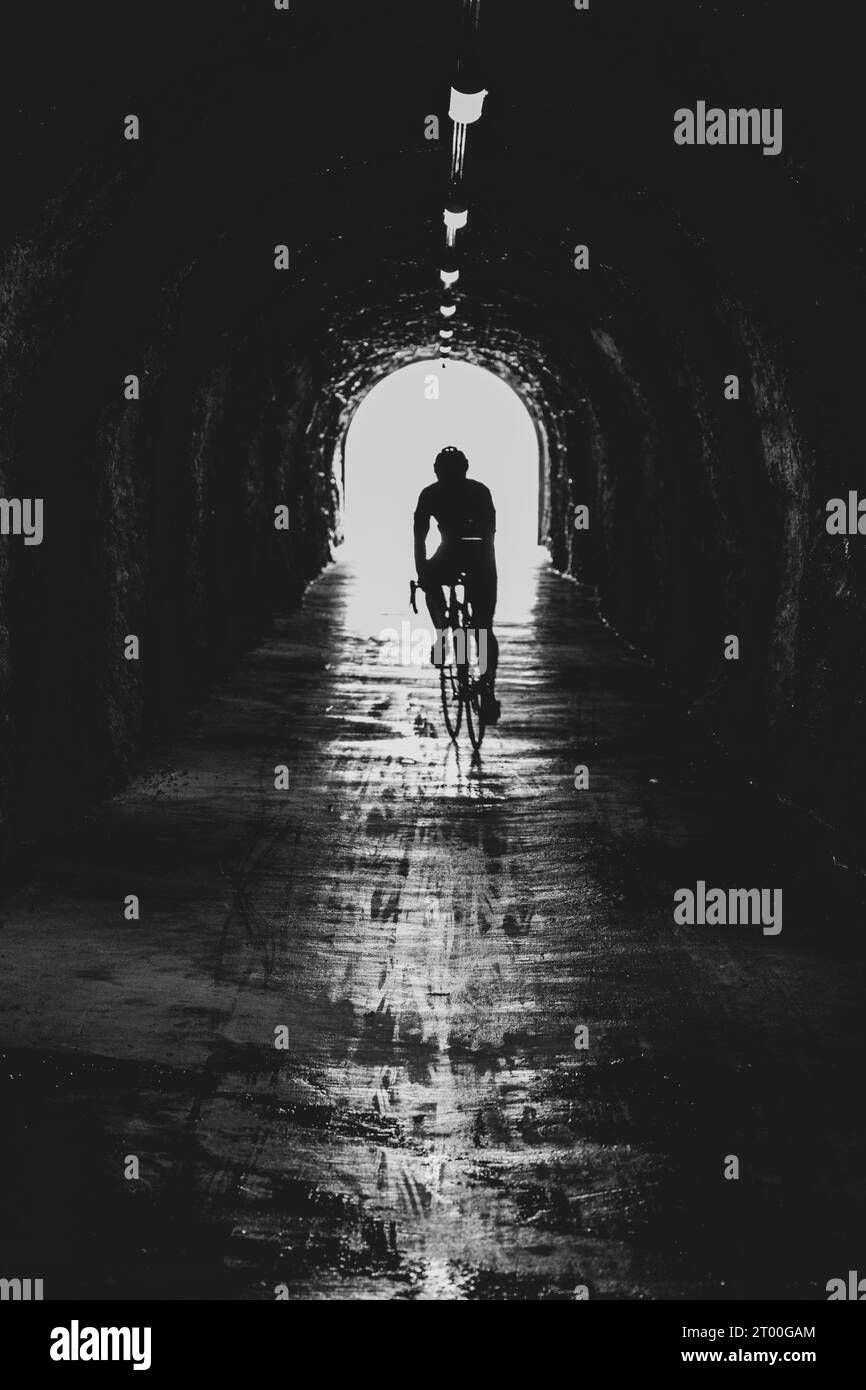 Ciclista en la bicicleta de carretera en el túnel estrecho. Silueta de atleta. Fotografía en blanco y negro. Foto de stock