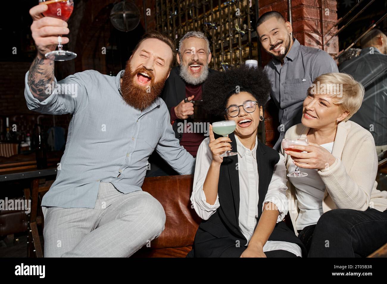 amigos multiétnicos emocionados sosteniendo bebidas y riendo en el bar de cócteles, divirtiéndose después del trabajo Foto de stock