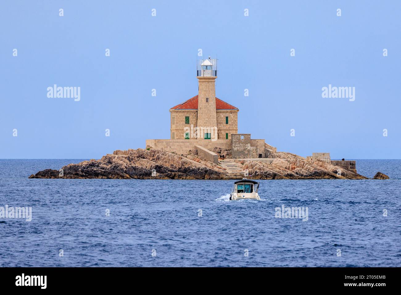 un pequeño barco taxi se acerca al faro de mulo en una pequeña isla rocosa en la costa croata Foto de stock