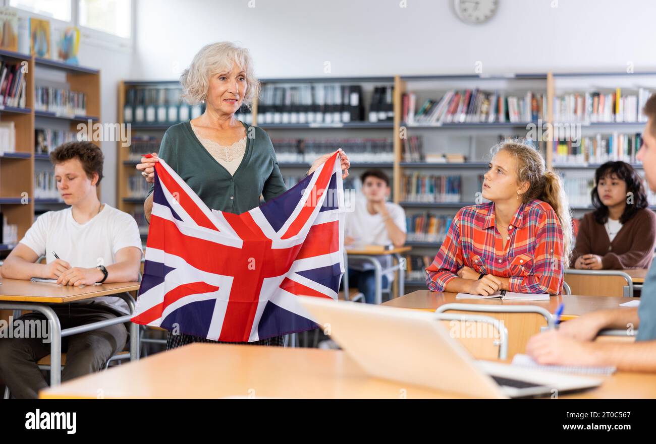 Profesora adulta discutiendo con los niños sobre la bandera nacional de Gran Bretaña en la lección de geografía en la biblioteca Foto de stock