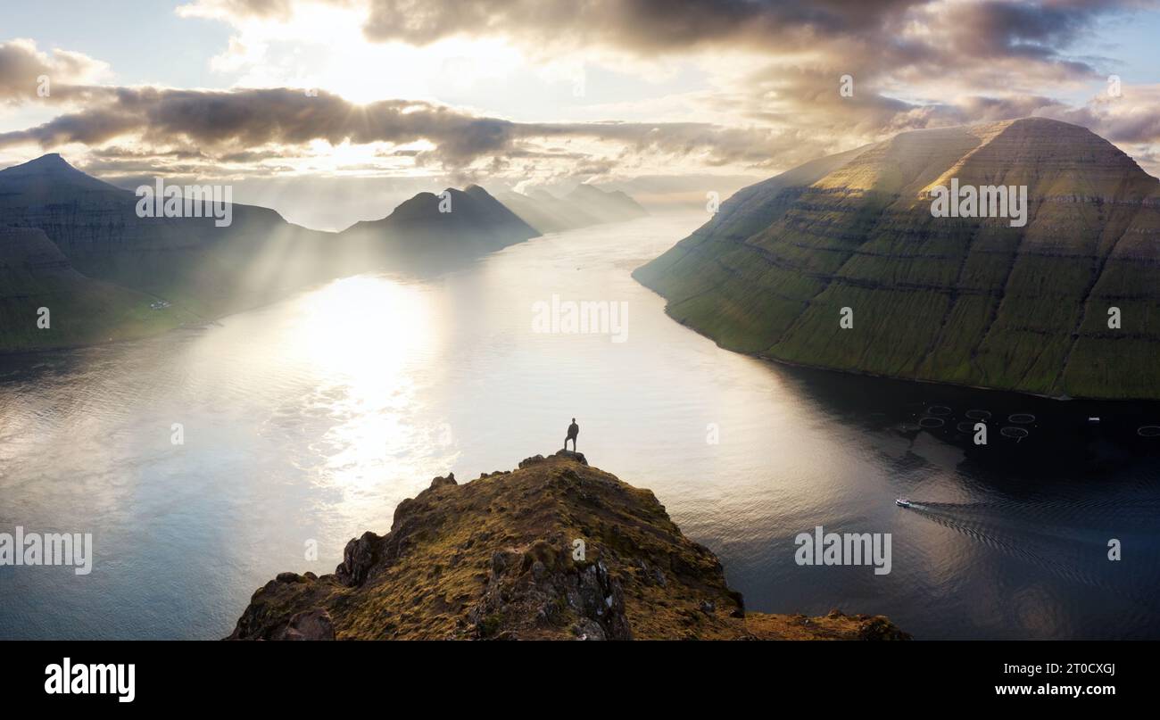 Silueta del hombre sobre la puesta del sol dramática con la montaña y el océano en las islas de Feroe cerca de Klaksvik Foto de stock