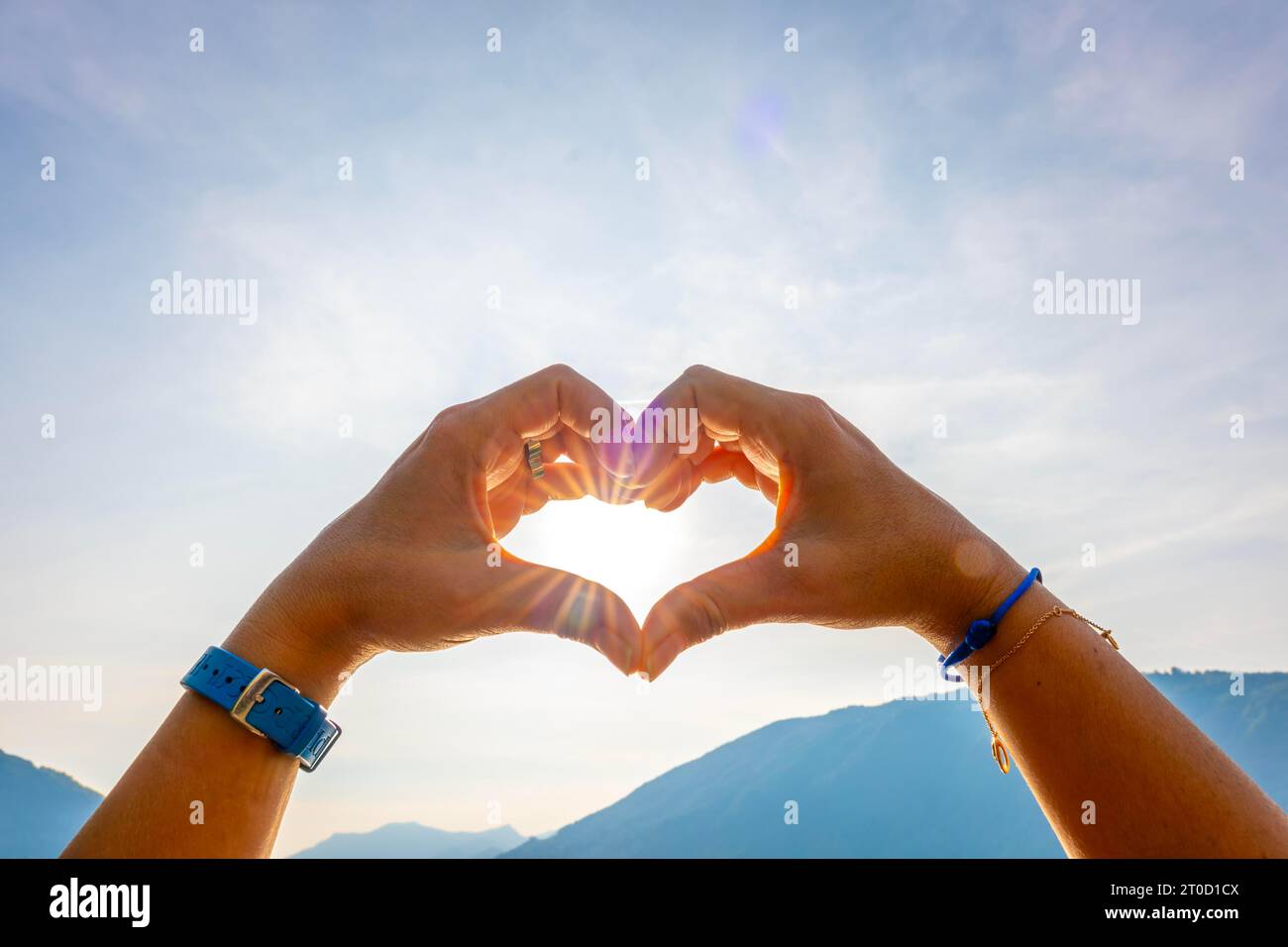 Manos de la mujer que hacen una forma del corazón contra el cielo con el sol y el rayo de sol y la montaña en Suiza Foto de stock