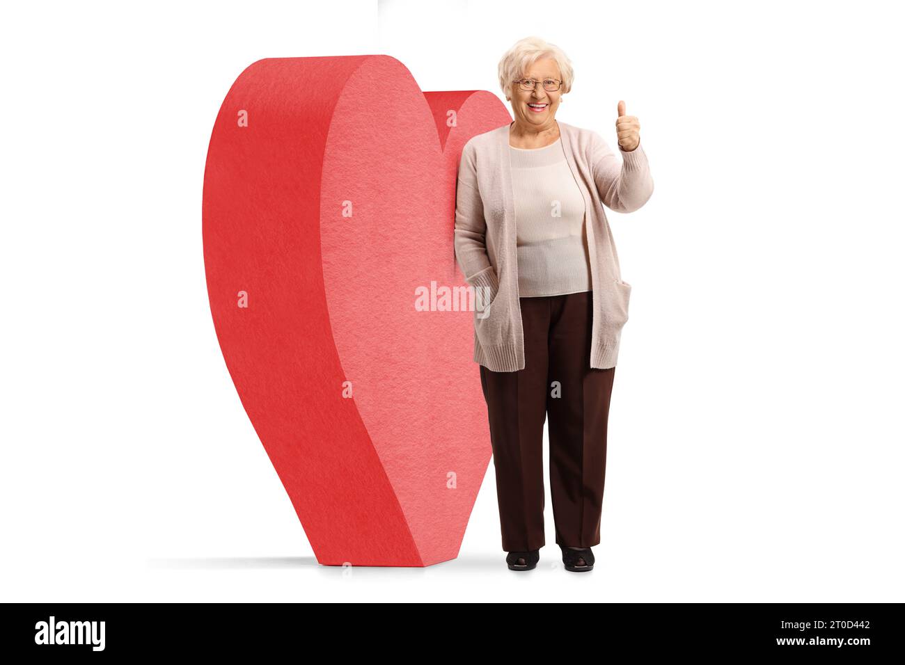 Retrato de cuerpo completo de una mujer mayor apoyada en un gran corazón rojo y pulgares gesticulantes para arriba aislados sobre fondo blanco Foto de stock