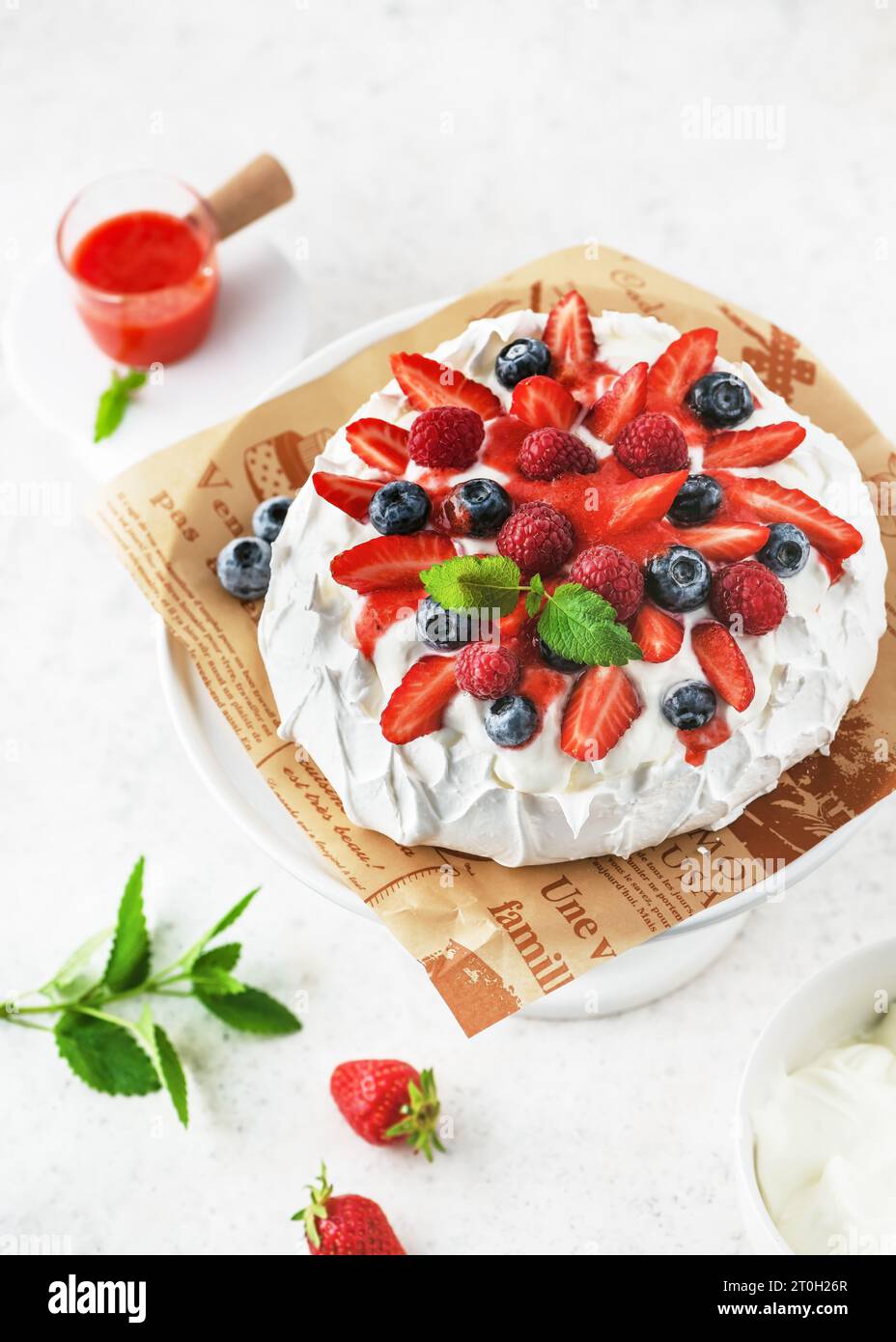Vista superior del delicioso pastel de merengue casero Pavlova con crema batida, fresas frescas, arándanos, frambuesas y salsa de fresa. Foto de stock