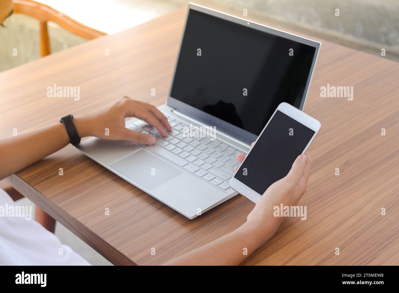 Cierre de la mano del hombre de negocios tocando la pantalla en blanco del teléfono móvil con el ordenador portátil al lado en la mesa. Pantalla de smartphone y portátil simulada Foto de stock