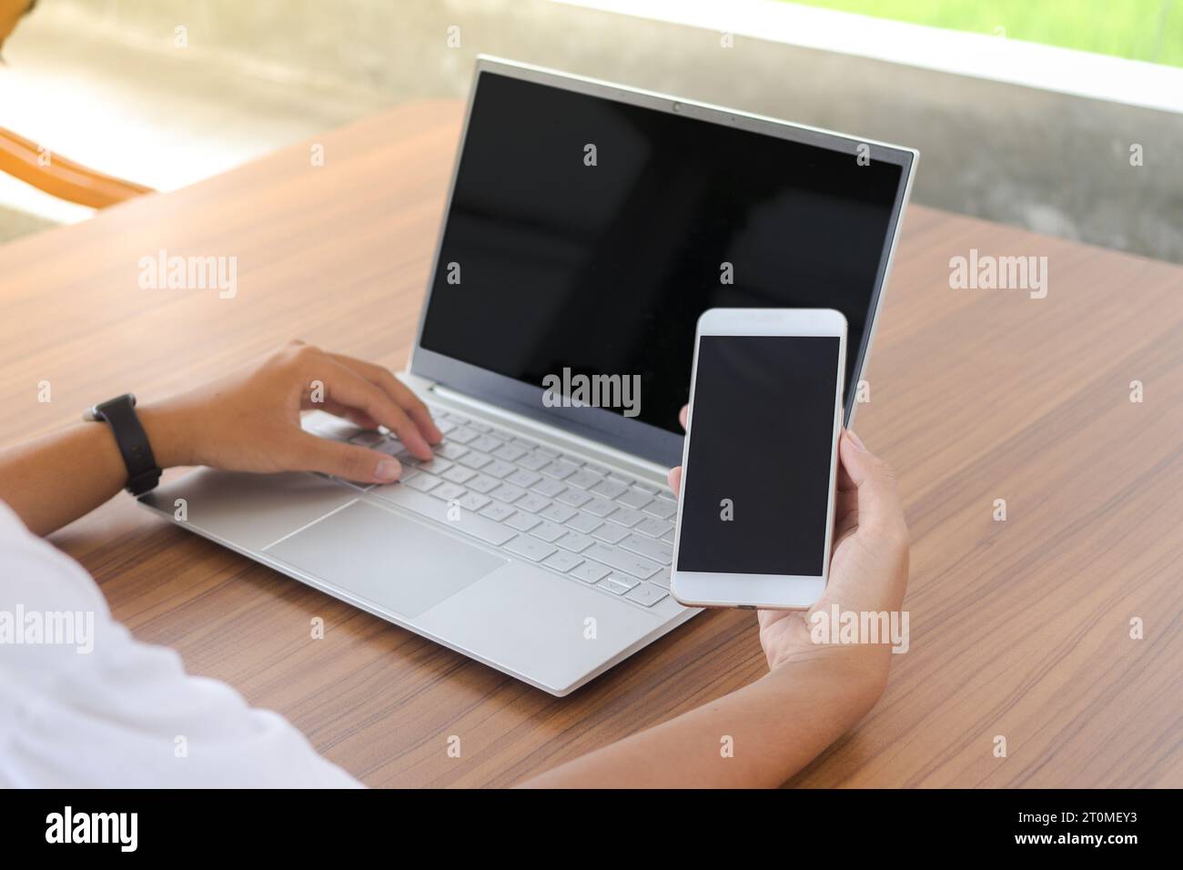 Cierre de la mano del hombre de negocios tocando la pantalla en blanco del teléfono móvil con el ordenador portátil al lado en la mesa. Pantalla de smartphone y portátil simulada Foto de stock