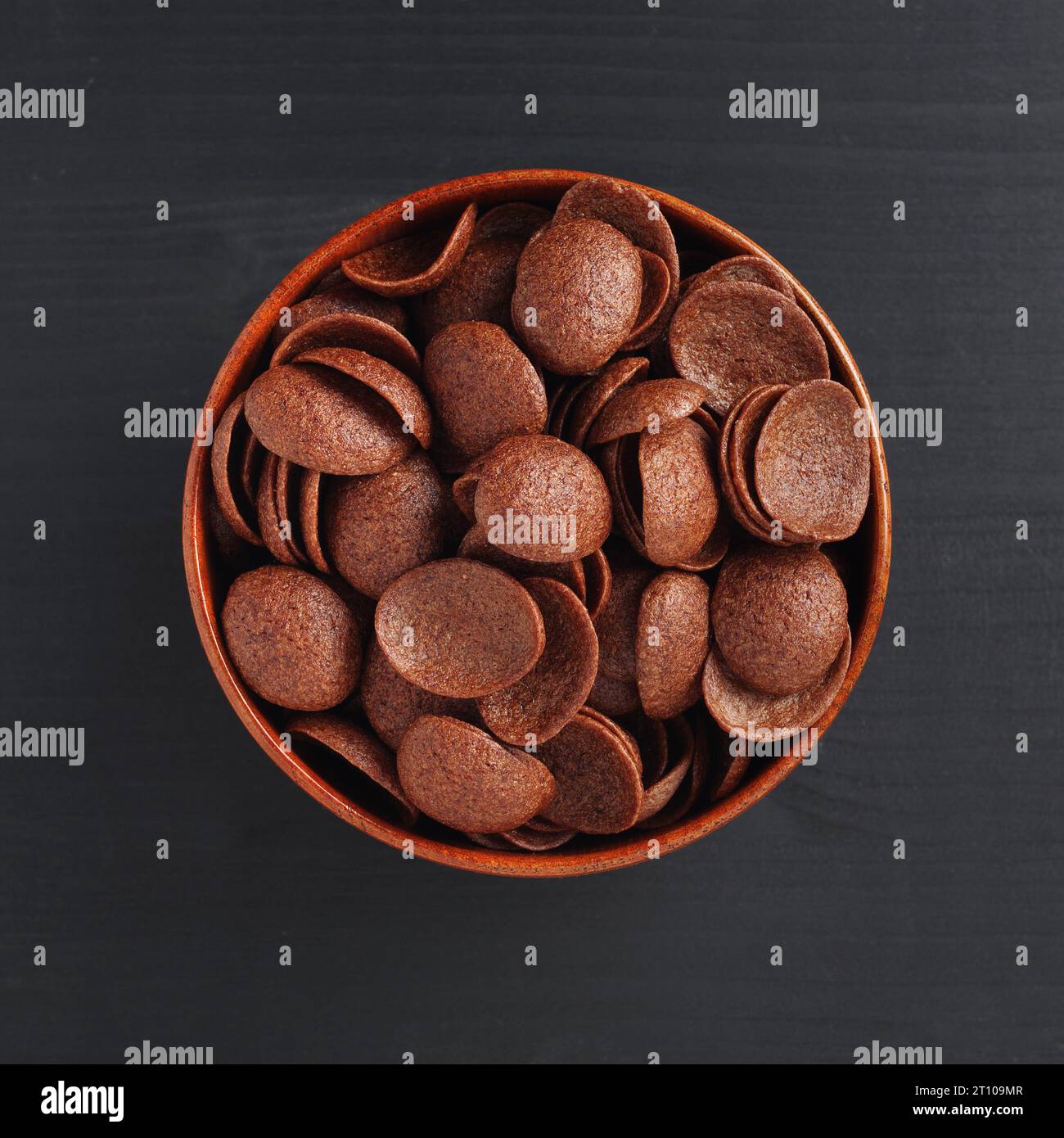 Directamente encima de la vista de los copos de maíz de chocolate en tazón sobre fondo de madera negro Foto de stock