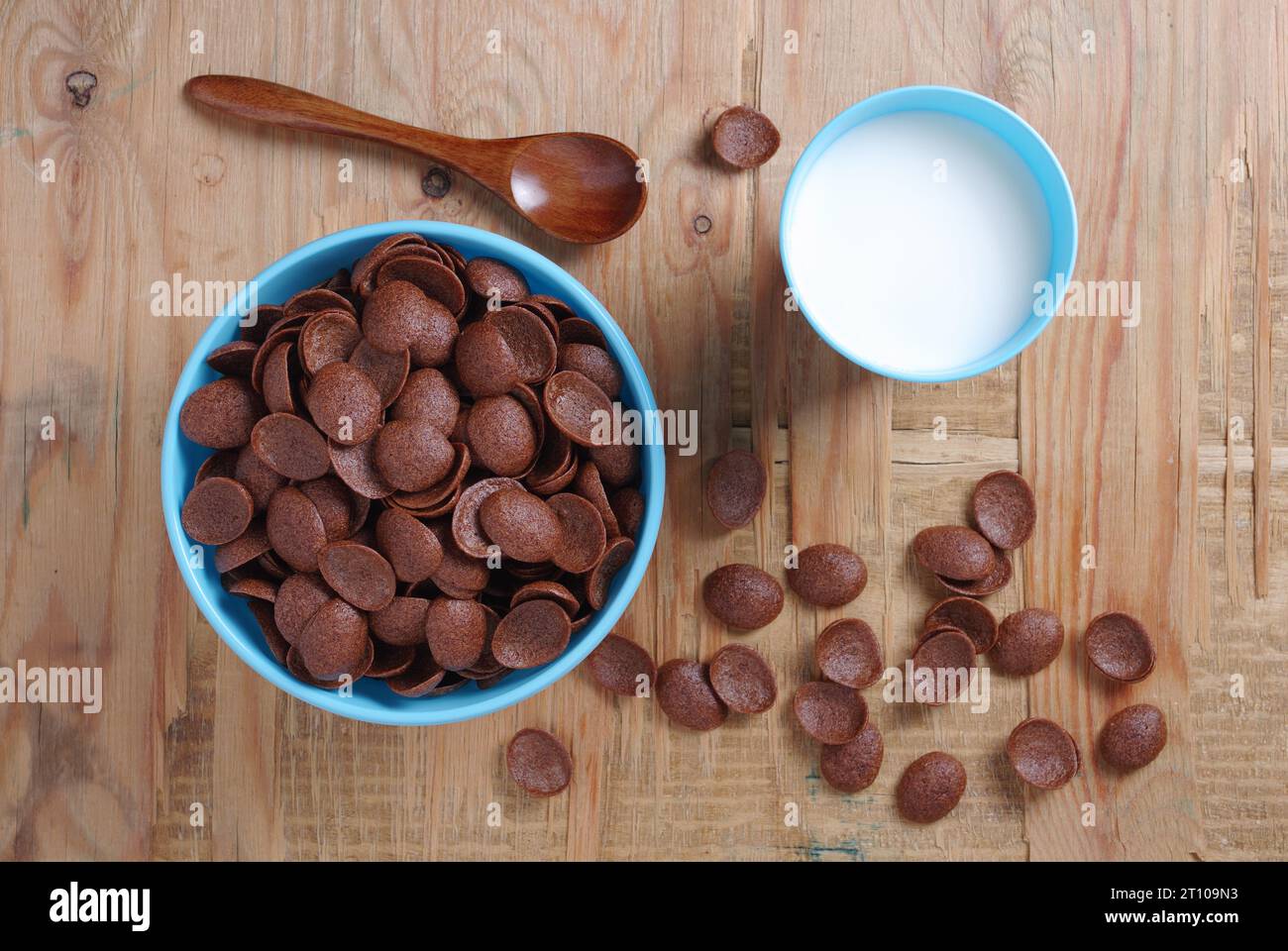Directamente encima de la vista de los copos de maíz de chocolate en tazón azul y vaso de plástico de leche de fondo de madera viejo Foto de stock