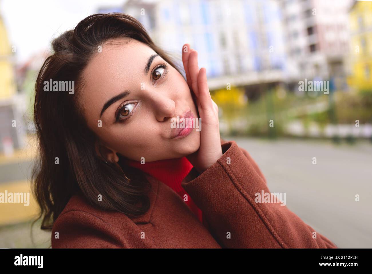 Mujer elegante joven linda en un abrigo marrón del otoño toma un selfie en la calle para su novio. Foto de stock