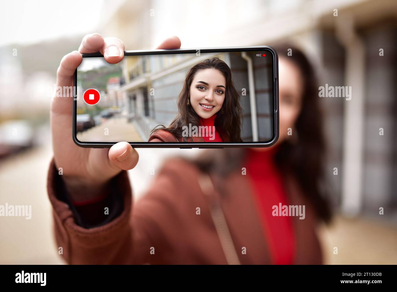 Una mujer joven en la calle está blogueando en video en su teléfono, su imagen visible en la pantalla del teléfono. Foto de stock