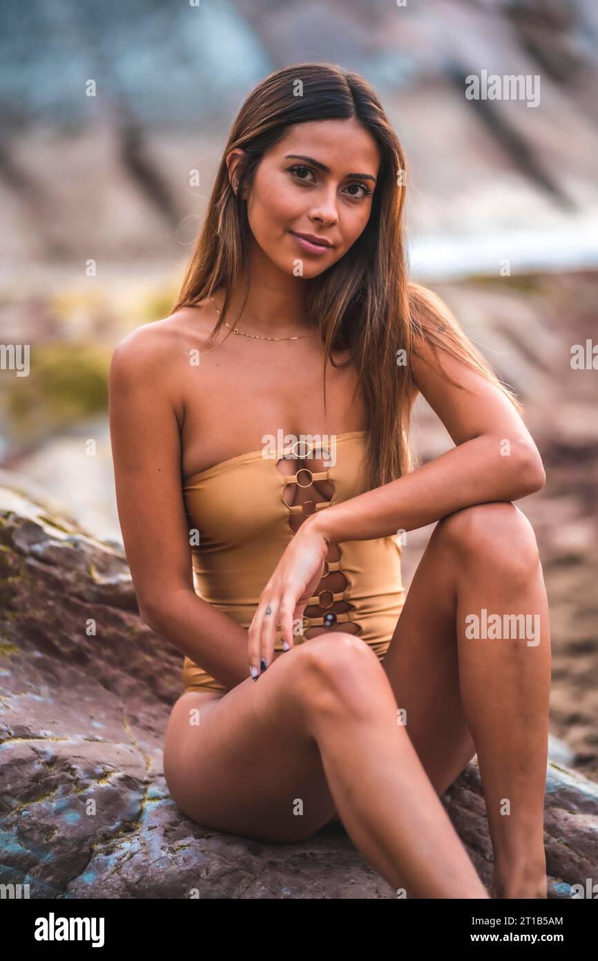 Retrato de una mujer morena con un traje de baño en las rocas de la playa en verano, mirando a la cámara Foto de stock