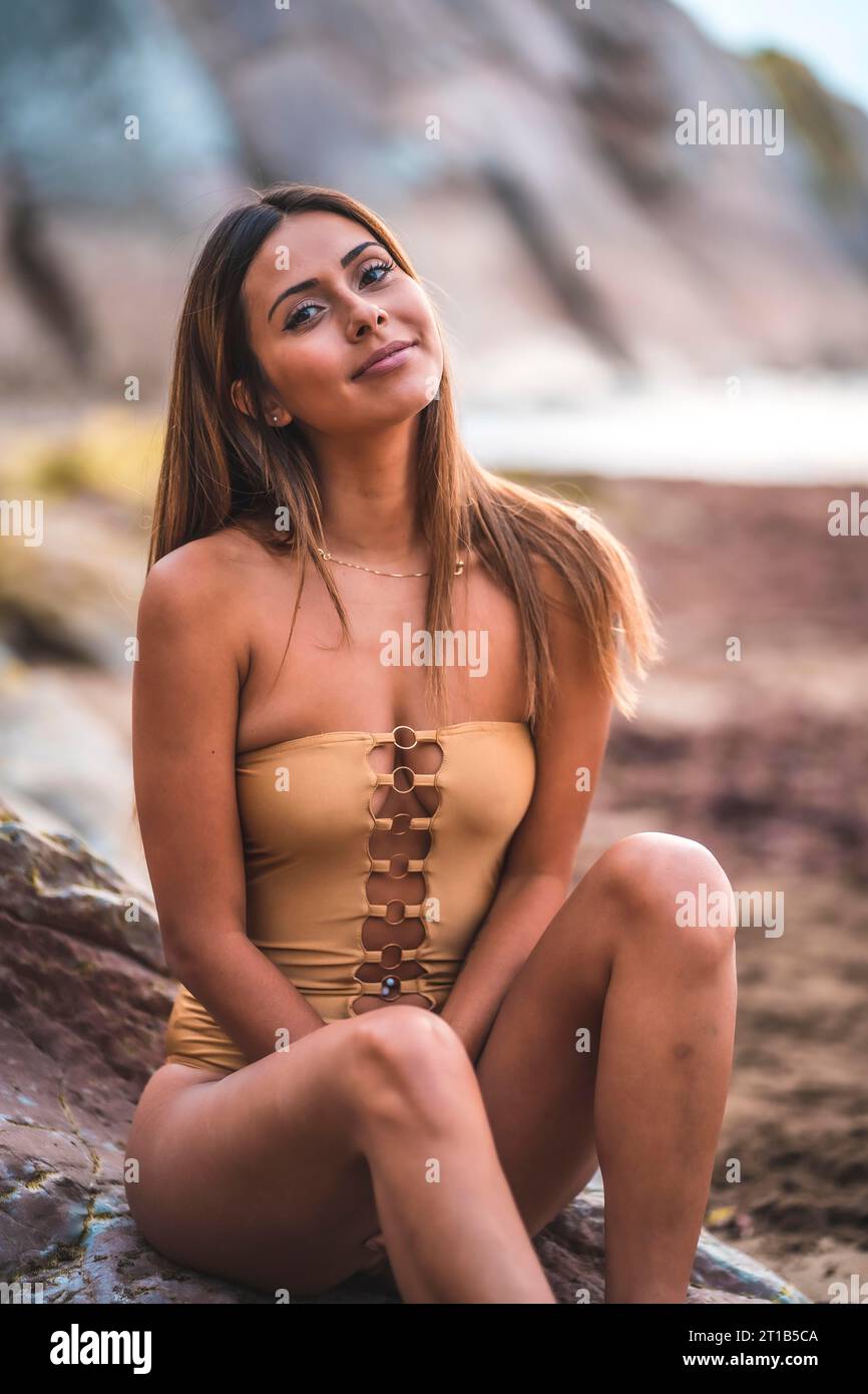 Retrato de una mujer morena sonriendo con un traje de baño en las rocas de la playa en verano, mirando a la cámara Foto de stock