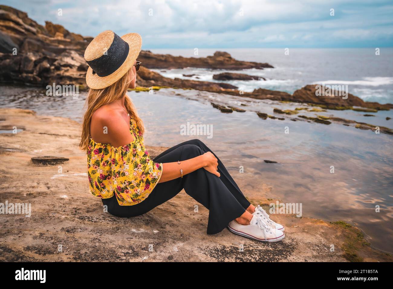 Chica de moda sentado mirando el mar azul en una hermosa tarde, con el mar  detrás