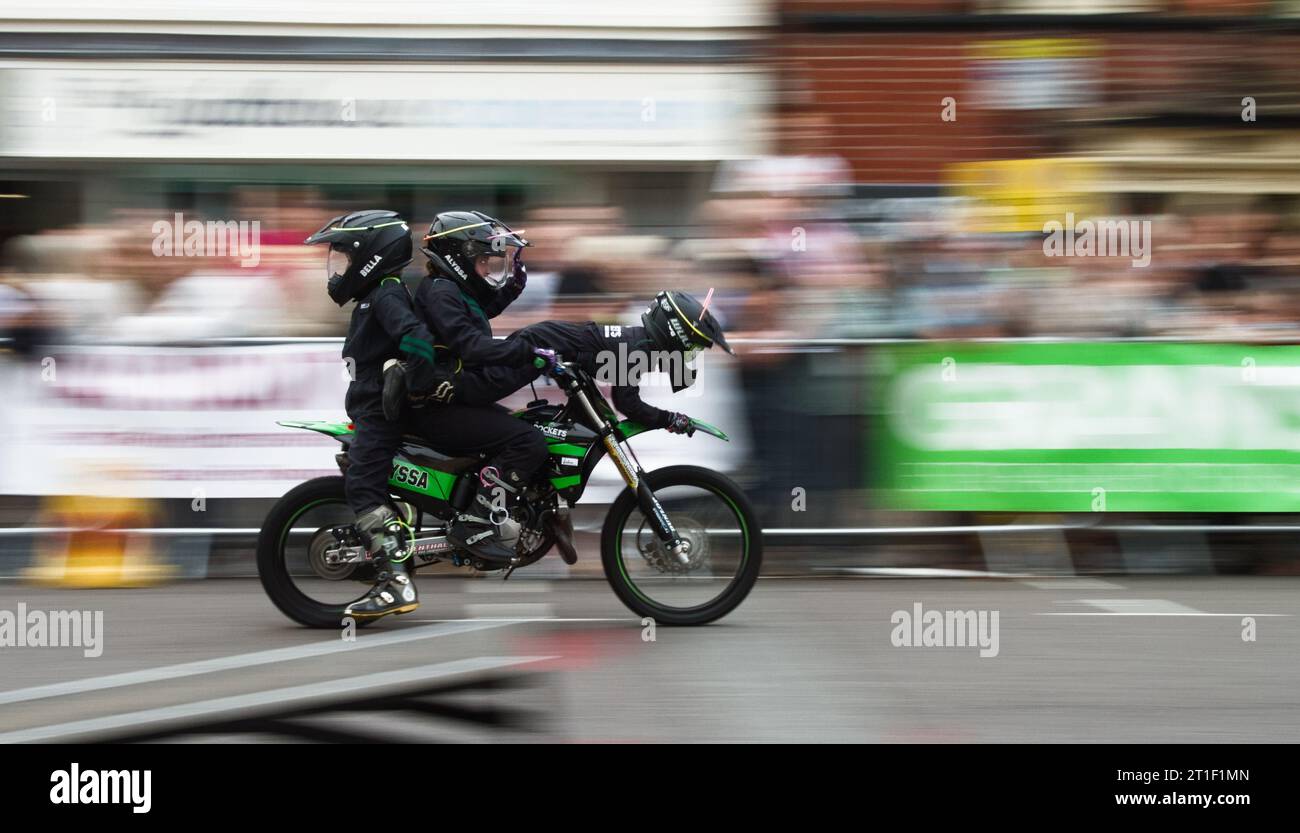 Tres miembros del equipo de exhibición de motocicletas para niños Rockets equilibrando juntos en una bicicleta con Motion Blur Showing Speed, Ringwood Carnival, Reino Unido Foto de stock