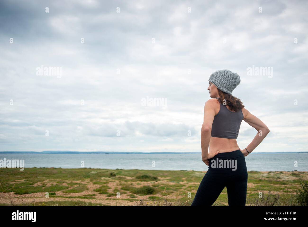Mujer deportiva descansando después de correr y hacer ejercicio afuera, mirando hacia el mar. Foto de stock