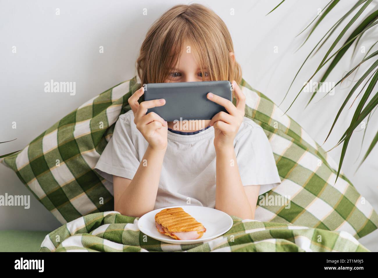 El joven, de unos 9-10 años, se encuentra en la cama, su largo pelo fluye, acunando una piña, simbolizando el ocio y un espíritu despreocupado Foto de stock