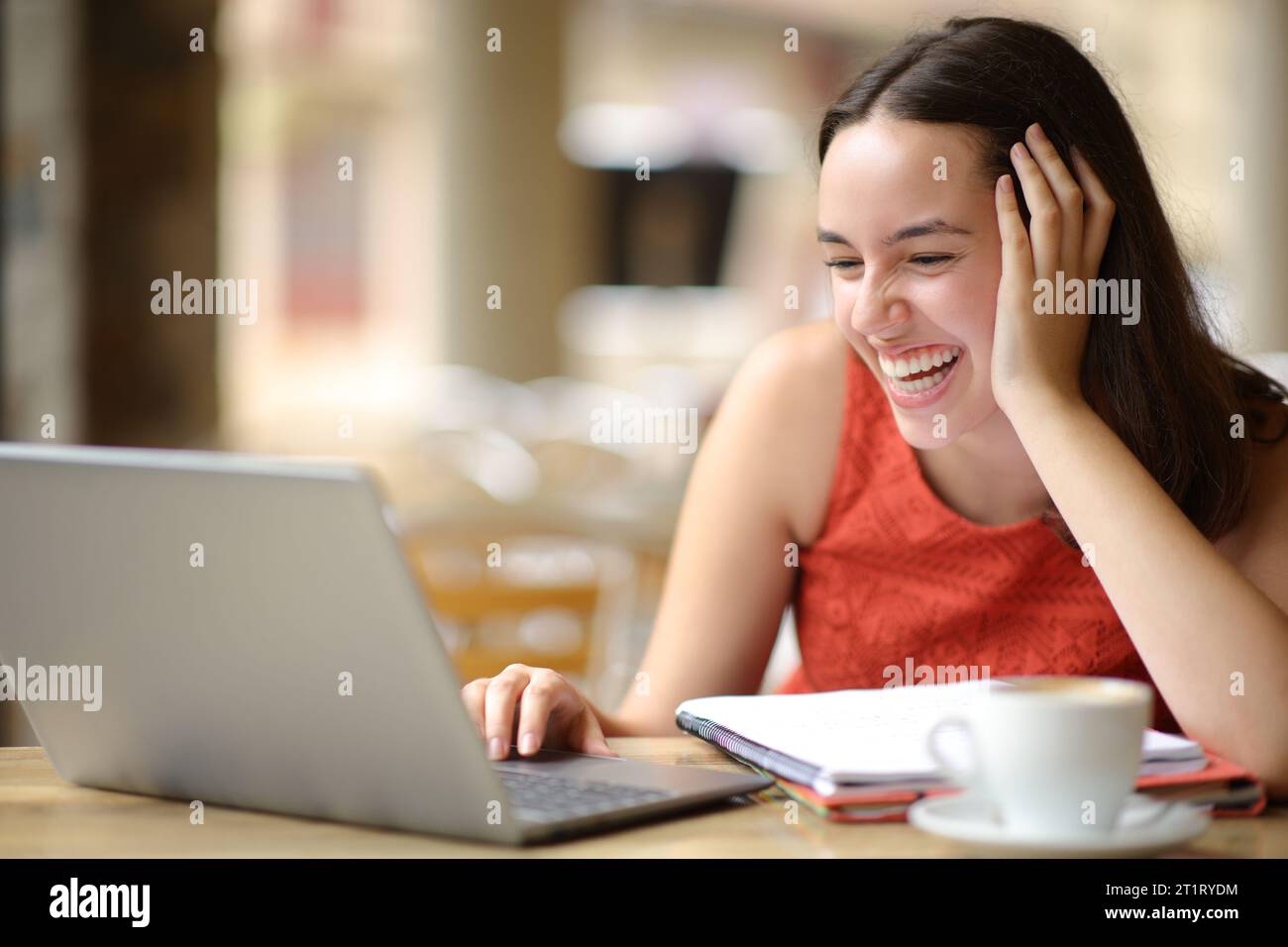 Estudiante feliz riendo ruidoso comprobando el ordenador portátil en una terraza de la cafetería Foto de stock