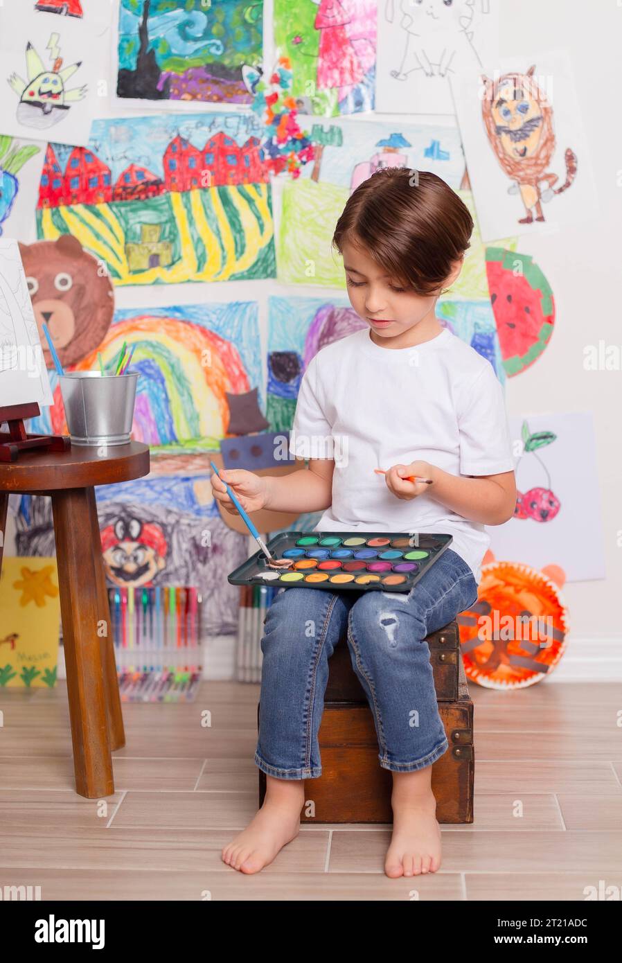 Un niño pequeño en un taburete mientras crea una obra maestra en un lienzo grande en un estudio de arte Foto de stock