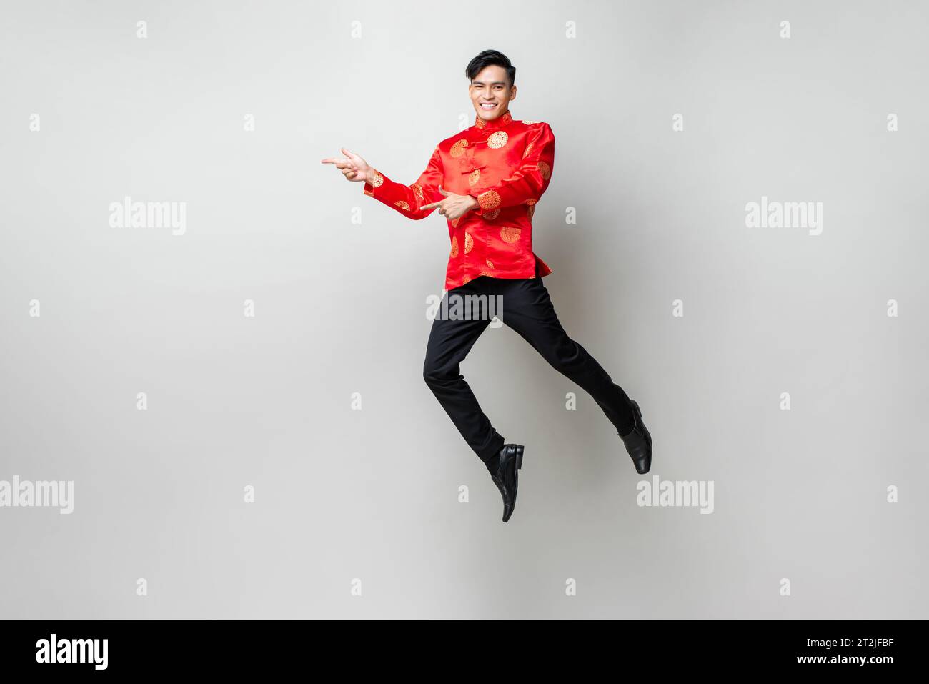 Retrato de un hombre asiático sonriente y guapo con atuendo chino tradicional sonriendo y apuntando con las manos a vaciar el espacio a un lado en la luz gris aislado estudio bac Foto de stock