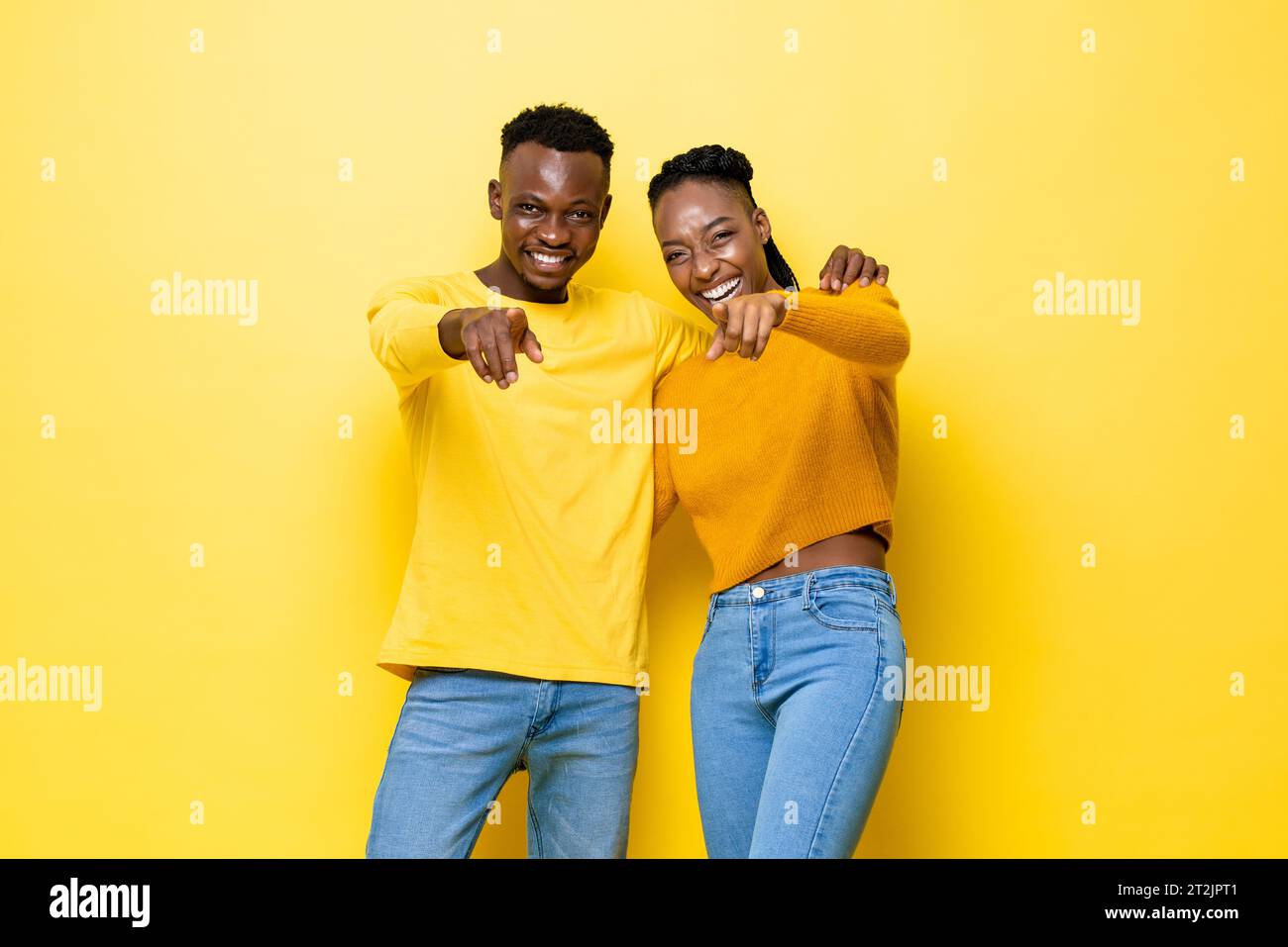 Joven feliz pareja africana apuntando a la cámara en el fondo amarillo aislado del stuido Foto de stock