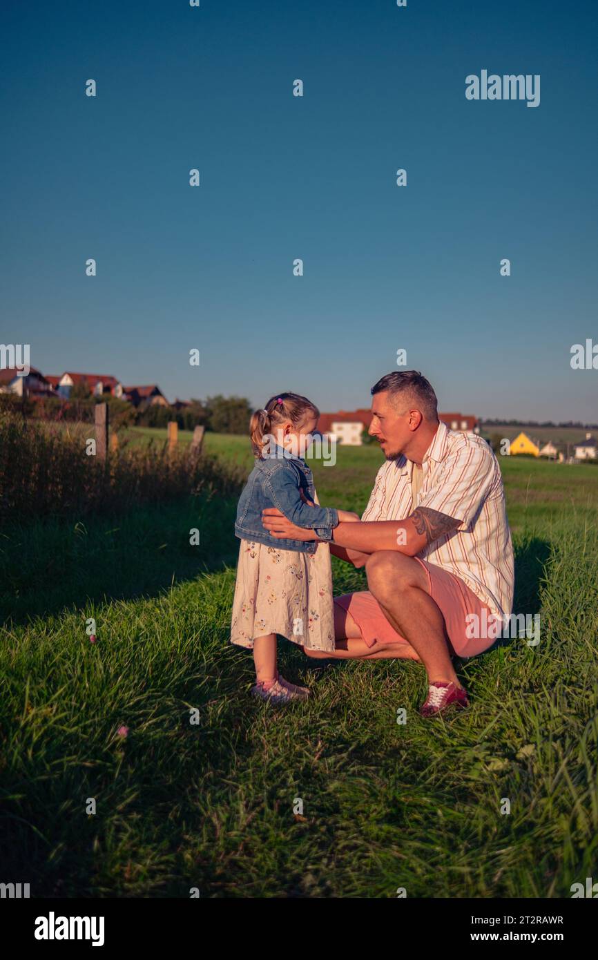 Papá e hija de apariencia caucásica caminando en un prado en un día soleado de verano al atardecer. Un hombre con su hija pasa tiempo jugando en la naturaleza. Foto de stock